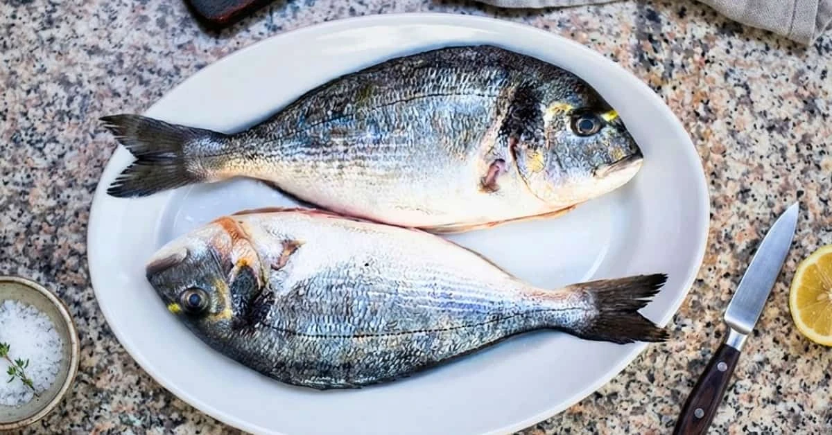 Deux poissons argentés entiers sur une assiette, avec un citron à côté